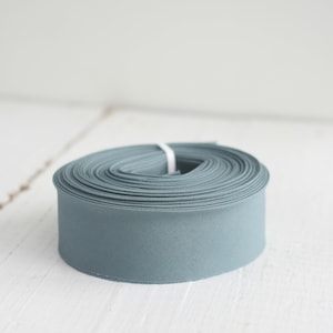 Puede incluir: Un rollo de cinta de tela azul claro, enrollado apretadamente y listo para usar para manualidades o decoración.