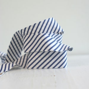 May include: A length of fabric ribbon featuring a repeating pattern of diagonal navy blue stripes on a white background. The ribbon is coiled into a loose, layered stack, displaying the consistent striped design across its entire visible surface.