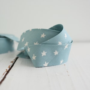 May include: A length of light blue fabric bias tape featuring a repeating pattern of small white five-pointed stars. The fabric strip is folded into a loose, overlapping coil, displaying the printed star design clearly across the surface.