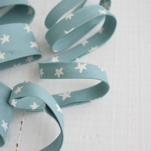 May include: Close-up of a light blue ribbon with a repeating pattern of white stars. The ribbon is curled and twisted, creating a decorative effect. The background is a white wooden surface.