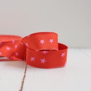 May include: A bright red ribbon featuring a repeating pattern of pink stars. The ribbon is curled, displaying the star design. This ribbon is suitable for crafts, gift wrapping, or general decorative use.