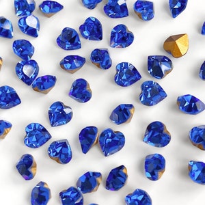 May include: A scattering of blue heart-shaped rhinestones with gold settings on a white background.