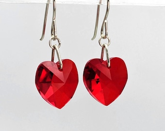May include: A pair of silver dangle earrings with red heart-shaped crystal drops.
