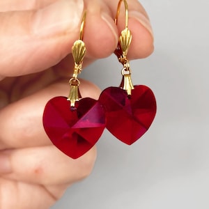 May include: A pair of gold heart-shaped earrings with red crystal accents.