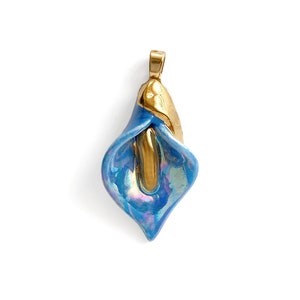 Puede incluir: Un colgante de cerámica azul y dorado en forma de flor. La flor tiene un centro dorado y pétalos azules iridiscentes.