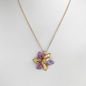 Puede incluir: Un collar de cadena dorada con un colgante de flor morado y dorado.