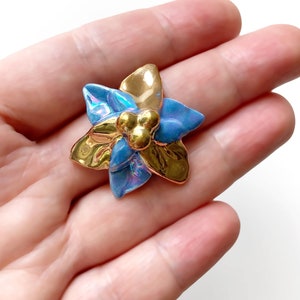 Op de afbeelding: Een blauwe en gouden keramische bloemenbroche met een textuur.