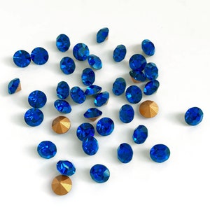 May include: A scattering of blue rhinestones with gold settings on a white background.