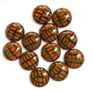 以下が含まれることがあります： オレンジと緑の模様が施された丸いボタンが12個。ボタンは幾何学的なデザインで、凹凸のある質感です。