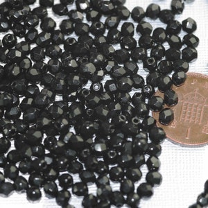 May include: A large pile of black faceted glass beads. The beads are approximately the size of a US penny.