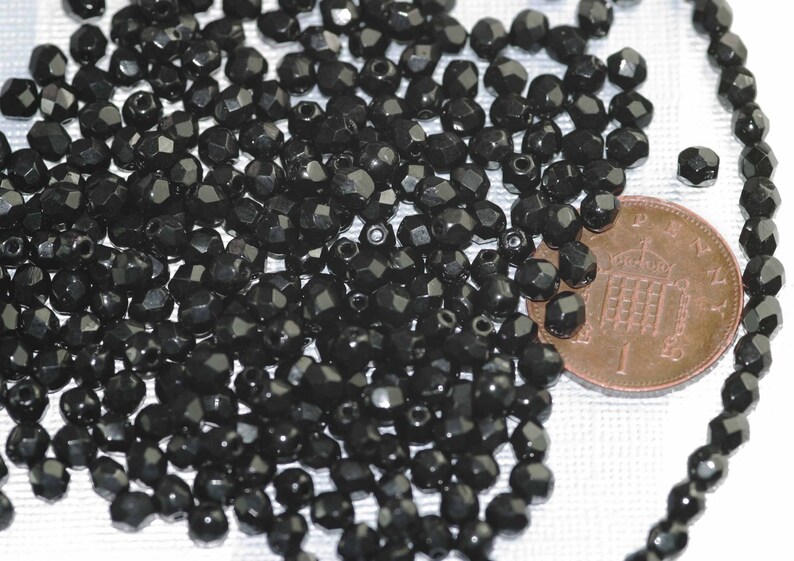 May include: A large pile of black faceted glass beads. The beads are approximately the size of a US penny.