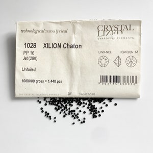 Puede incluir: Un paquete de 1.440 cristales negros Xilion Chaton de Swarovski. El paquete est&aacute; etiquetado con el n&uacute;mero de producto 1028, PP 16, Jet (280), Unfoiled y 10/00/00 gross = 1.440 pcs. El paquete tambi&eacute;n incluye un c&oacute;digo de barras y el logotipo de Swarovski.