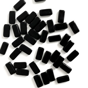 May include: A collection of small, rectangular black tiles with a smooth, glossy finish. Each piece features rounded corners and a uniform, solid black colour, scattered across the frame in various orientations and positions.