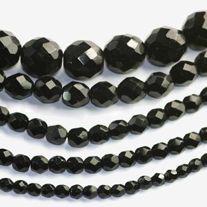 May include: A close-up of five strands of black faceted glass beads. The beads are arranged in rows, with the largest beads at the top and the smallest beads at the bottom.