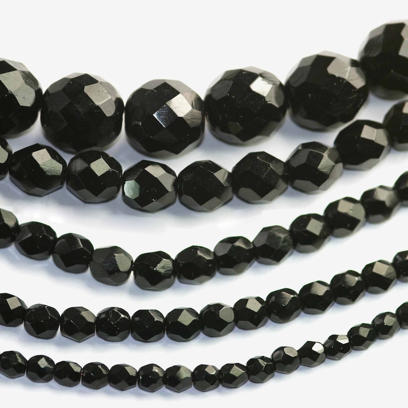 May include: A close-up of five strands of black faceted glass beads. The beads are arranged in rows, with the largest beads at the top and the smallest beads at the bottom.