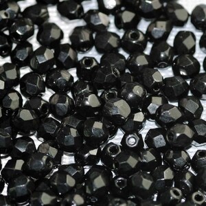 May include: A close-up of a large quantity of black faceted beads. The beads are scattered on a white surface.