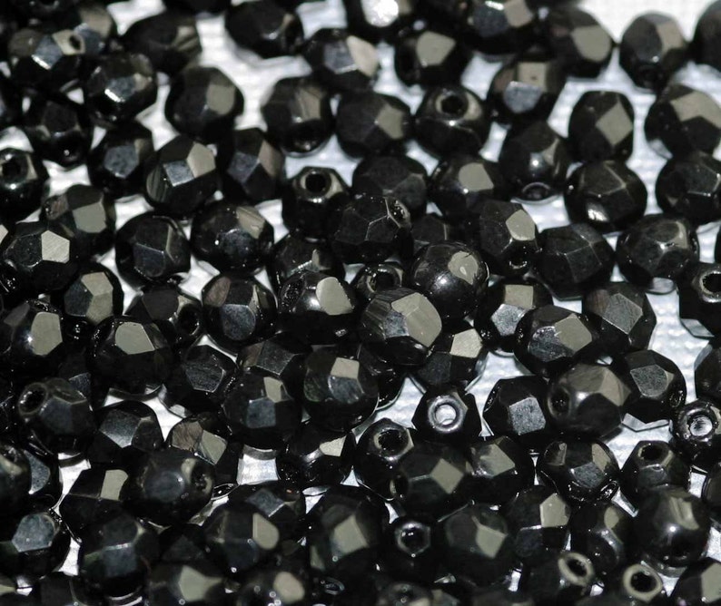 May include: A close-up of a large quantity of black faceted beads. The beads are scattered on a white surface.
