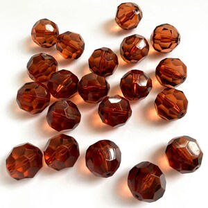May include: A collection of seventeen round, faceted beads in a translucent amber-brown color. Each bead features a multi-faceted surface that reflects light, creating a sparkling effect. The beads are scattered across the frame, showing a hole.
