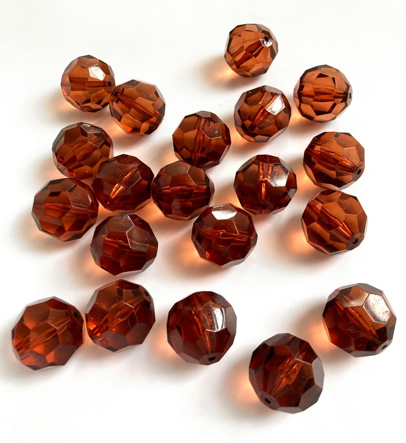 May include: A collection of seventeen round, faceted beads in a translucent amber-brown color. Each bead features a multi-faceted surface that reflects light, creating a sparkling effect. The beads are scattered across the frame, showing a hole.