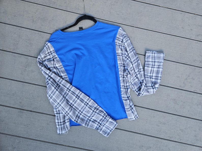 Pu&ograve; includere: Una maglia a maniche lunghe con un pannello centrale in jersey blu brillante, a contrasto con le maniche e i pannelli laterali caratterizzati da un motivo a quadri bianco, grigio e nero. Il capo &egrave; appeso a una gruccia in plastica nera.