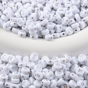 May include: White round beads with silver letter imprints, scattered across a white surface. The beads are uniform in size and shape, with a small hole for stringing. Ideal for jewelry making and crafts.