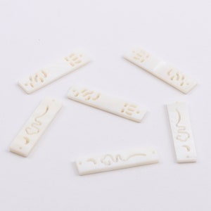 Può includere: Sei pezzi rettangolari bianchi di madreperla con intricati disegni ritagliati. I pezzi sono disposti in modo sparso su uno sfondo bianco.