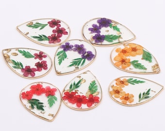 May include: A collection of teardrop-shaped resin pendants with gold-colored edges. Each pendant features colorful dried flowers and gold leaf accents. The flowers are in shades of red, purple, and orange, with green leaves.
