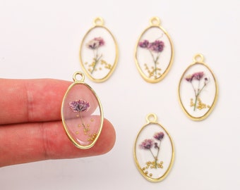 May include: Oval-shaped resin pendants with gold-colored frames. Each pendant features a dried purple flower and small gold-colored beads encased in clear resin, perfect for jewelry making or crafting.