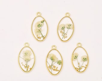 May include: Five gold oval-shaped charms with a clear resin insert containing dried white flowers and gold beads.