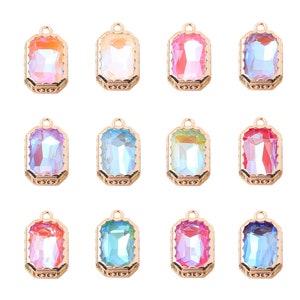 Może przedstawiać: Kolekcja dwunastu prostokątnych wisiorków z kamieniami szlachetnymi w różnych kolorach, w tym pomarańczowym, różowym, niebieskim i fioletowym. Każdy wisiorek ma złotą ramkę z filigranu i małą pętelkę u góry do zawieszenia.