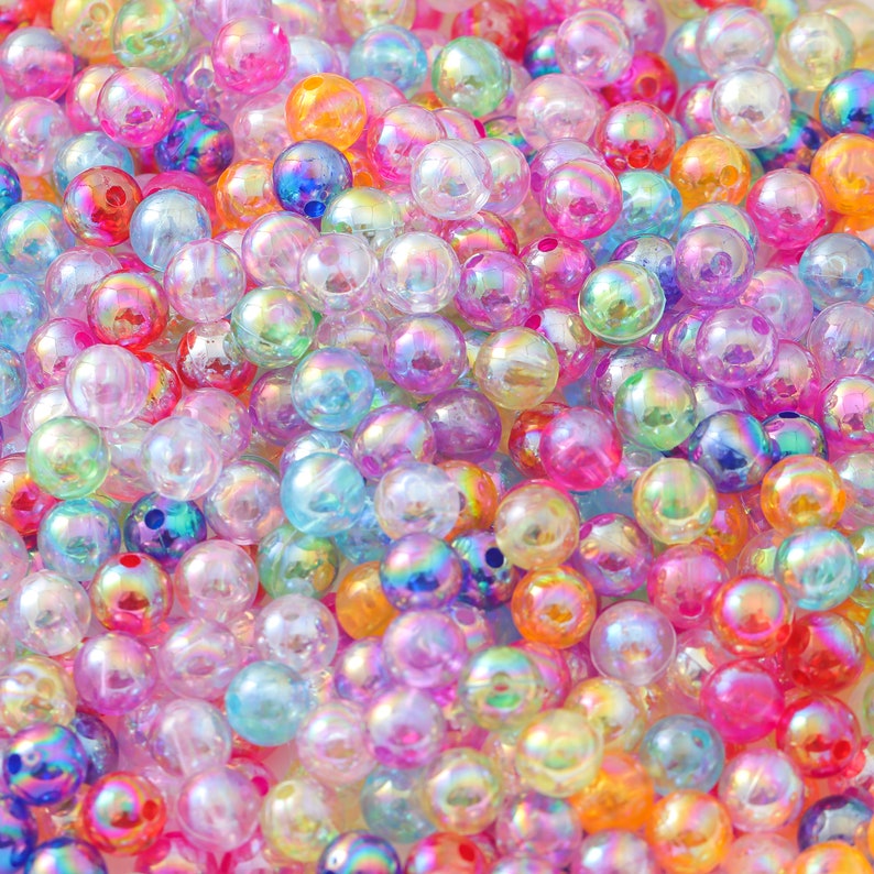 May include: A large pile of iridescent rainbow colored plastic beads. The beads are round and have a smooth, shiny finish.