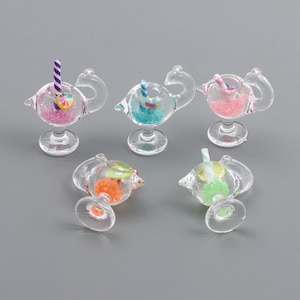 May include: Five miniature glass cocktail glasses with colourful straws and decorative fruit. The glasses are shaped like a flamingo and have a clear base.