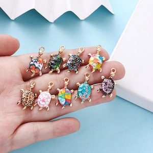 May include: A selection of colourful turtle charms with gold-coloured accents. The charms display diverse patterns, including floral, leopard print, and geometric designs. Each charm has a small loop for attaching to jewellery or other crafts.