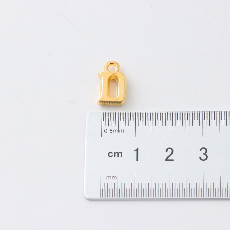 May include: Gold-colored metal letter D charm pendant. The charm is approximately 1 cm in height.