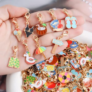 May include: A collection of gold-tone metal charms featuring colourful enamel summer-themed designs including ice cream, a bikini, a coconut drink, a sand bucket, flip-flops, swim trunks, a unicorn float, a beach umbrella, and a beach sign.