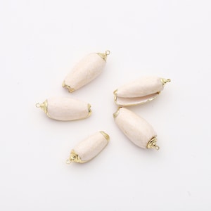 Könnte beinhalten: Fünf weiße Muscheln mit goldenen Akzenten. Die Muscheln sind oval geformt und haben eine strukturierte Oberfläche. Sie haben eine goldene Schlaufe oben zum Aufhängen.