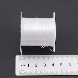 Puede incluir: Un carrete de hilo el&aacute;stico transparente, que mide 6 cm de largo, con una etiqueta blanca que dice "0,5 mm".