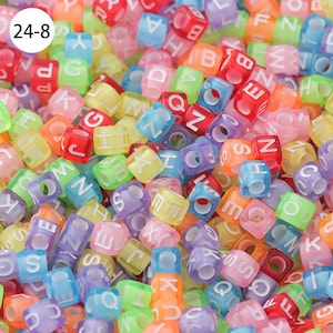 May include: A close-up of a large pile of colorful alphabet letter beads. The beads are made of translucent plastic and have white letters on them. The beads are in a variety of colors, including red, orange, yellow, green, blue, purple, and pink.