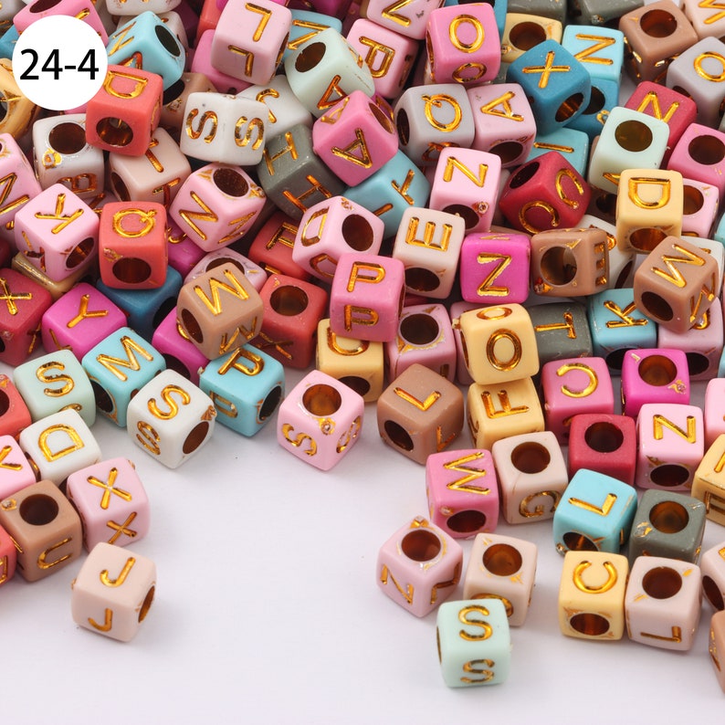 May include: A large pile of colorful alphabet letter beads with gold lettering. The beads are made of plastic and have a hole in the center for stringing.