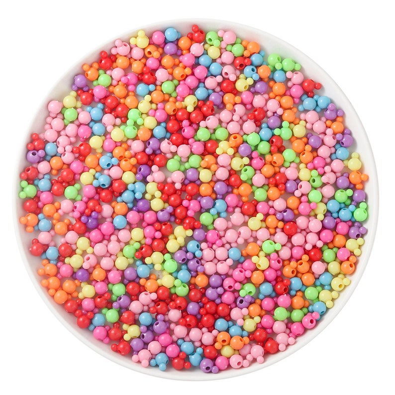 May include: A bowl filled with colorful plastic beads in various shades of pink, purple, blue, green, yellow, orange, and red. The beads are shaped like Mickey Mouse heads.