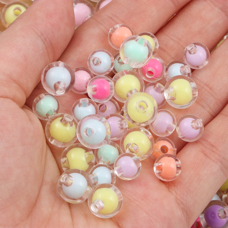May include: A handful of colorful beads in pastel shades of pink, yellow, blue, green, and orange. Each bead has a smaller, solid-colored sphere encased in a clear, transparent outer shell. These beads are ideal for jewelry making and crafts.