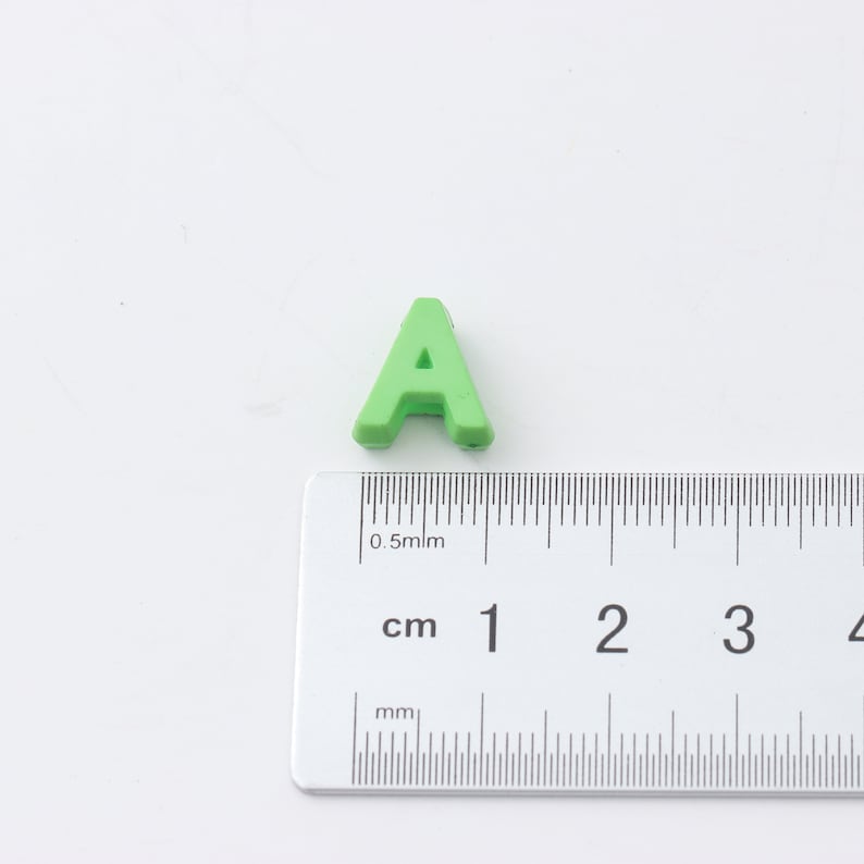 May include: A green plastic letter A, measuring approximately 1 cm in height, is placed next to a ruler.