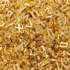 May include: A large pile of gold-colored metal letter charms. The charms are all different letters of the alphabet.