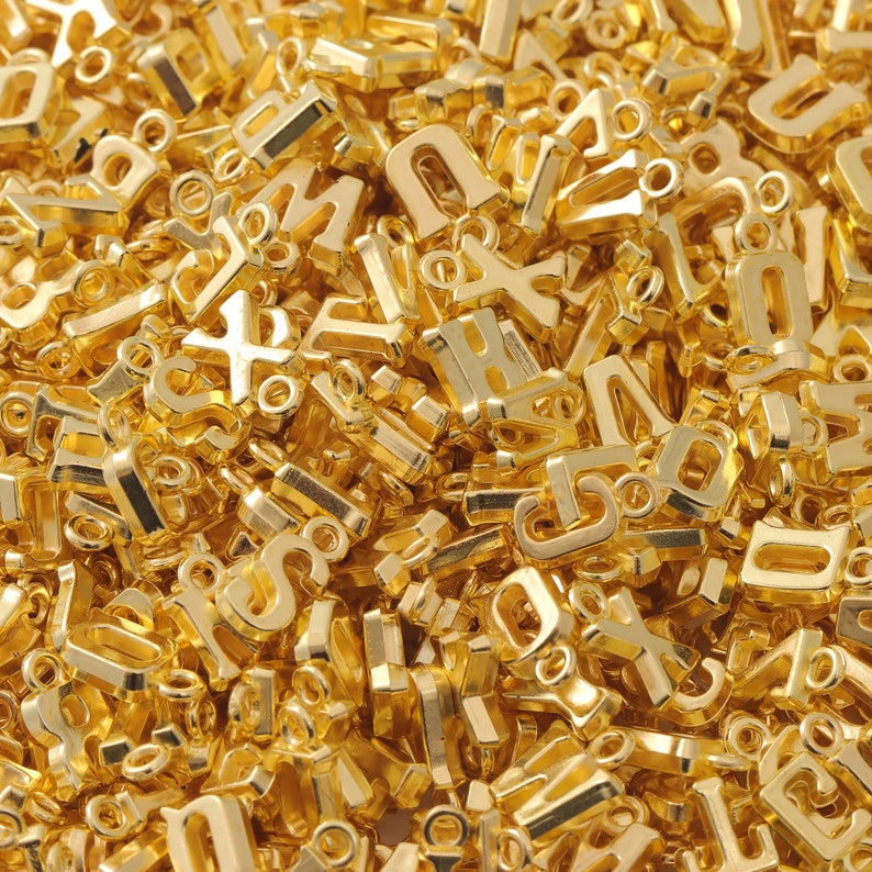 May include: A large pile of gold-colored metal letter charms. The charms are all different letters of the alphabet.