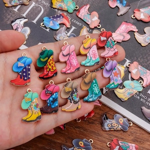 May include: A selection of vibrant cowboy boot charms in shades of red, pink, blue, and yellow. Each charm has detailed designs and a gold-coloured loop for attaching to jewellery or crafts. The charms are shown against a patterned background.