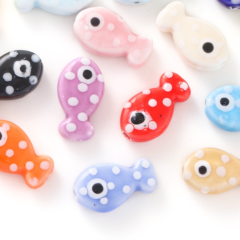 Pode incluir: Conjunto de contas de peixe de vidro coloridas com bolinhas brancas e olhos pretos. As contas s&atilde;o de v&aacute;rias cores, incluindo rosa, roxo, vermelho, laranja, azul e amarelo.