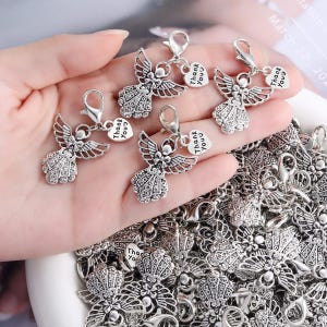 Puede incluir: Una colección de dijes de ángel de metal en tono plateado, cada uno con detalles intrincados de filigrana en las alas y el vestido. Cada dije incluye un cierre de langosta y una pequeña etiqueta en forma de corazón grabada con Thank You.