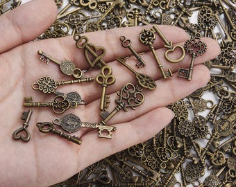 May include: A collection of antique bronze-colored keys with ornate designs, including heart, scroll, and fleur-de-lis shapes. The keys vary in size and detail, suggesting a vintage or steampunk aesthetic. Some keys are held in a hand, while others are scattered.