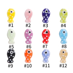 Pode incluir: Doze pingentes de peixe de cer&acirc;mica com corpos de diferentes cores e bolinhas brancas. Cada peixe tem um olho preto e um c&iacute;rculo branco no centro do olho. Os peixes s&atilde;o numerados de 1 a 12.