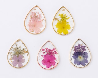 May include: Five teardrop-shaped resin pendants with gold trim, each containing a different pressed flower arrangement. The flowers are pink, yellow, purple, and red.